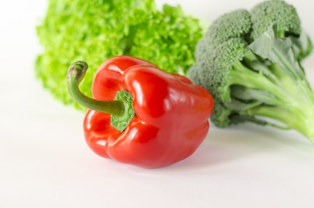 Juicy red pepper with a green tail lies next to Bundle of lettuce and broccoli are on a white background. isolatedの写真素材