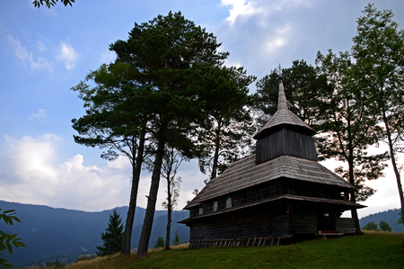 Old wooden Ukrainian Church stands high in the mountains surrounded by old tall treesの写真素材