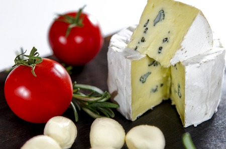 Assorted cheeses on wooden board. Camembert, cheese with blue mildew, mozzarella with tomatoes and rosemaryの写真素材