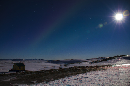 The moon with the rays and the Aurora in Iceland s blue winter sky over an Icelandic house that stands on a lava field covered with snow.の写真素材
