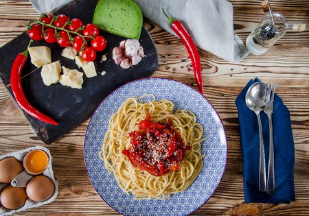 Parmesan, cherry tomatoes, chilli peppers, green cheese and garlic lie on a dark board that stands on a wooden table next to a beautiful plateの写真素材