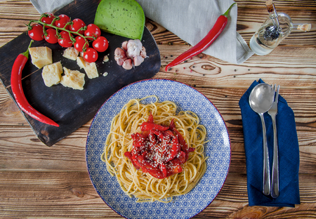 Parmesan, cherry tomatoes, chilli peppers, green cheese and garlic lie on a dark board that stands on a wooden table next to a beautiful plateの写真素材