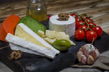 Mix cheese on dark background on wood board with grapes, honey, nuts, tomatoes and basil. Top view.の写真素材