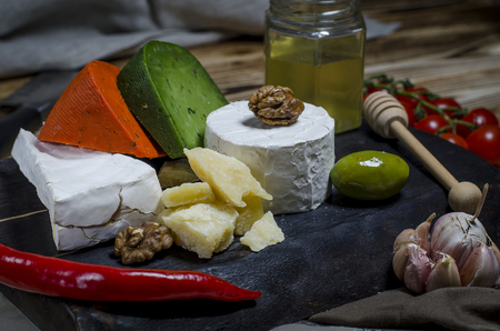Mix cheese on dark background on wood board with grapes, honey, nuts, tomatoes and basil. Top view.の写真素材