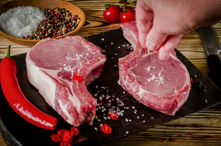 hand salt meat steak. Raw marbled meat steak, pepper, herbs, garlic, old wooden background. Space for text. Beef Rib eye steak ready for cooking.の写真素材