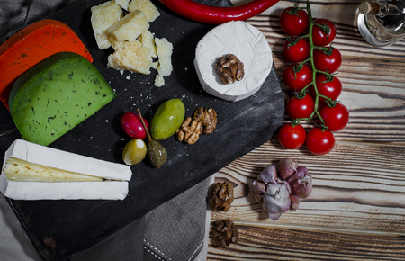 Mix cheese on dark background on wood board with grapes, honey, nuts, tomatoes and basil. Top view.の写真素材