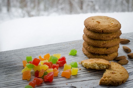 Round orange biscuits with colorful candied fruits and a slice of juicy orange lying on a wooden table against the background of winter forestの写真素材