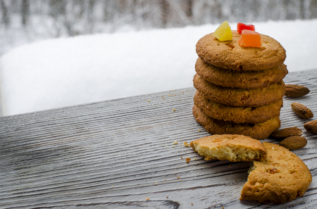 Round orange biscuits with colorful candied fruits and a slice of juicy orange lying on a wooden table against the background of winter forestの写真素材