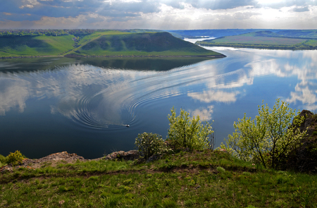 The huge river Dniester flows between high steep hills covered with spring lush green grass against the blue skyの写真素材