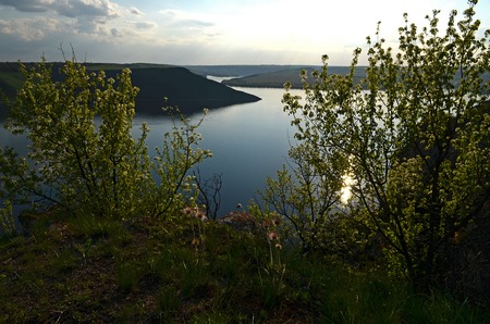 The huge river Dniester flows between high steep hills covered with spring lush green grass against the blue skyの写真素材