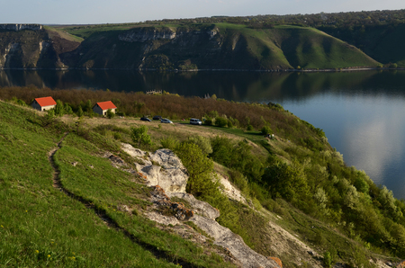 The huge river Dniester flows between high steep hills covered with spring lush green grass against the blue skyの写真素材