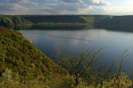 The huge river Dniester flows between high steep hills covered with spring lush green grass against the blue skyの写真素材