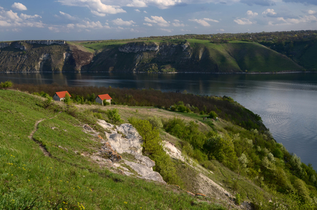 The huge river Dniester flows between high steep hills covered with spring lush green grass against the blue skyの写真素材