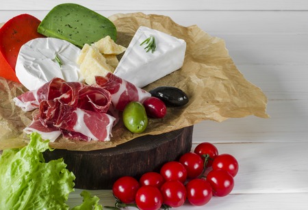 Mix cheese and meat on white background on wood board with grapes, honey, nuts, tomatoes and basil. Top view.の写真素材