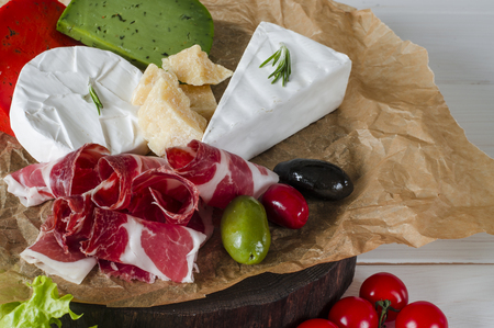 Mix cheese and meat on white background on wood board with grapes, honey, nuts, tomatoes and basil. Top view.の写真素材