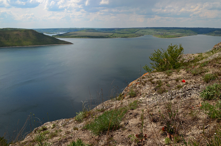 The huge river Dniester flows between high steep hills covered with spring lush green grass against the blue skyの写真素材