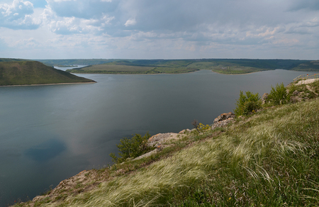 The huge river Dniester flows between high steep hills covered with spring lush green grass against the blue skyの写真素材