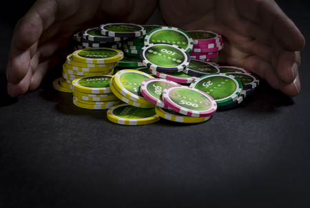 On the black table lie poker chips, cards and a dealer chip. Man's hand holds cardsの写真素材