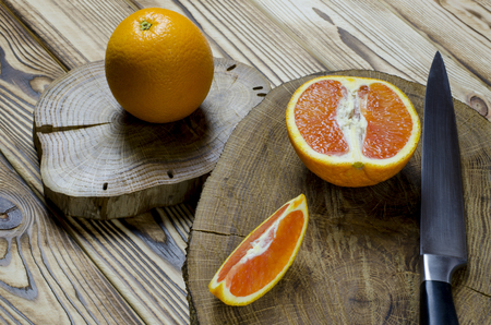 cut Sicilian oranges and knife with black knob rests on a wooden board, which stands on a wood tableの写真素材