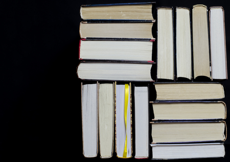 Many multicolored thick open books stand on a dark background. On the books are old round glasses and an open notebook with a pencil. ready to readの写真素材