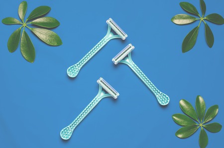 shaving razor lie on the colored background next to green leaves. Top view, flat layの写真素材