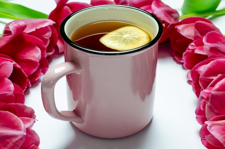 Pink Cup of Tea with lemon stands on a white background next to pink tulips. closeupの写真素材