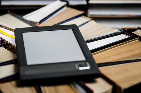 The e-book with a white screen lies on the open multi-colored books that lie on a dark background,...