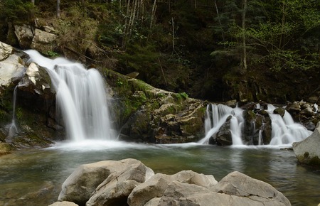 Forest flowing waterfall high up in the mountains of the Carpathians with noise flows down on a background of green forestの写真素材