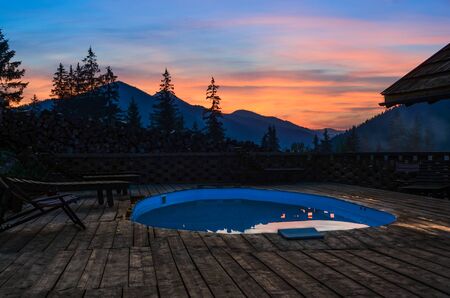 Oval open-air swimming pool high in the mountains against the backdrop of the beautiful summer sunset and mountains. The Carpathians. Ukraineのeditorial素材
