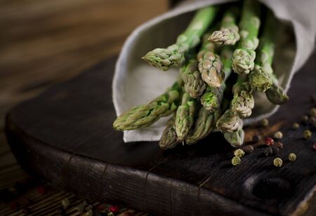Green juicy asparagus is lying on a wooden dark board on a brown wooden table. copy spaceの写真素材