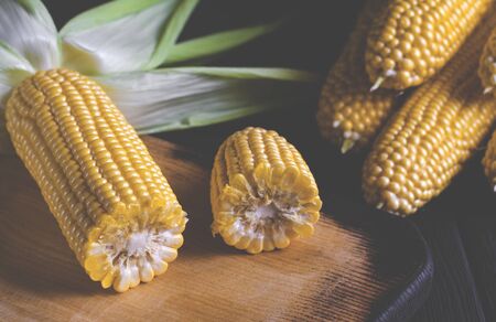 Yellow juicy corn with green leaves on a black tree table. Close-up