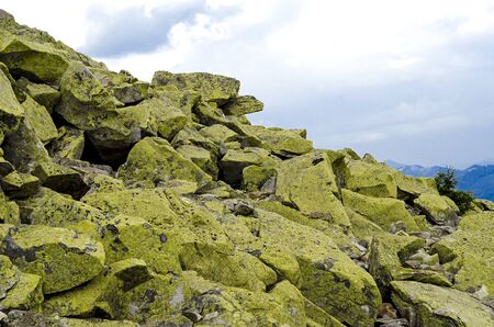 Huge stones with green lichen lie on top of the mountain against the backdrop of high ridges and blue skyの写真素材