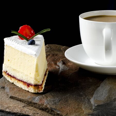 Fruit cake with cherries, grapes and plum stands on a wild stone next to a white cup of coffee with...