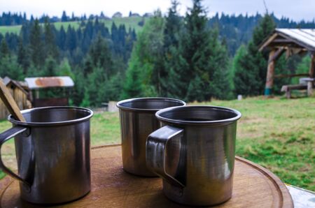 Three metal cups with morning coffee in the campaign against the background of the mountains covered with forests