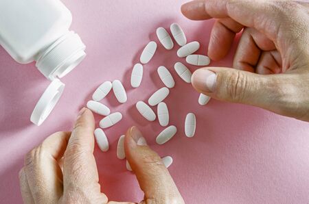 A white plastic container with white tablets lies on a multi-colored background next to white tablets. Close-upの写真素材
