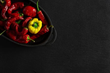 Dried multi-colored, textured chili peppers lie in black form for baking on a black stone background. Close-upの写真素材