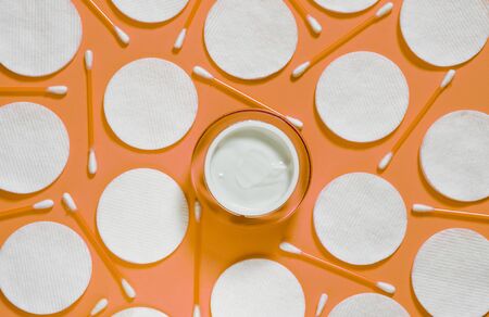 Hygiene products: white round cotton pads and plastic sticks for cleaning the ears lie on a pink background next to face cream. Top view, flat layの写真素材