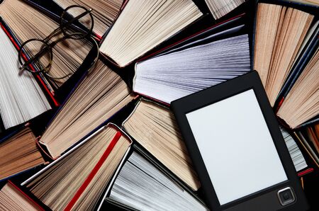 The e-book with a white screen lies on the open multi-colored books that lie on a dark background, ready to read. close-upの写真素材