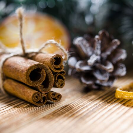 Christmas card: cinnamon and a slice of lemon is lying on a brown wooden background next to the pine conesの写真素材