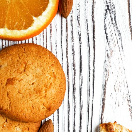 Orange biscuits lie on a white wood background with orange wedge and almonds. flat layの写真素材