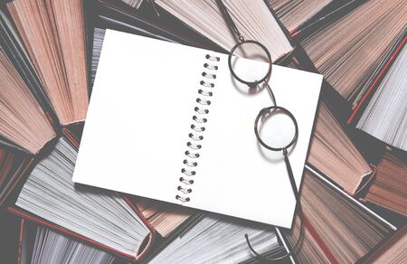 Many multicolored thick open books stand on a dark background. On the books are old round glasses...