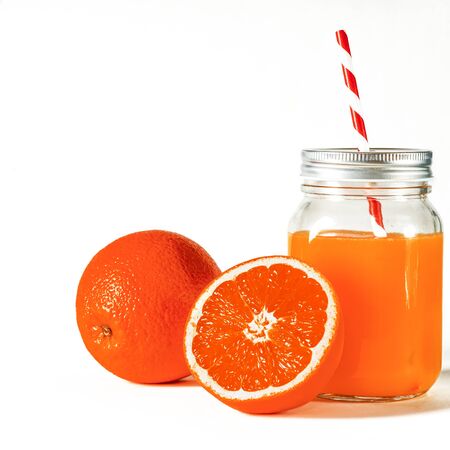 Glass jar with a tube with freshly squeezed orange juice stands on a white background next to fresh oranges. isolatedの写真素材