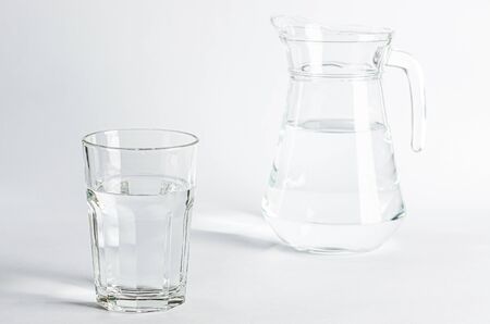 Pure clear water in a glass glass and glass jug stands on a white background. isolatedの写真素材