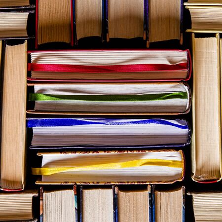 Lots of colourful thick open books stand on a dark background. ready to read