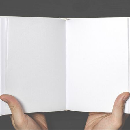 Men's hands hold a white book with clean pages. Mockup of closed blank square bookの写真素材