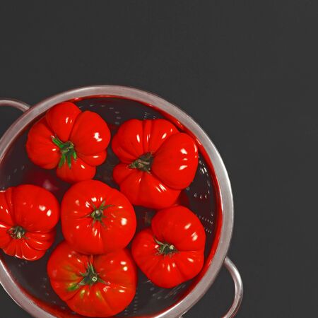 Red washed tomatoes lie in a metal bowl, which stands on a black background. Close-up