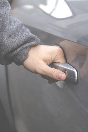 The man's hand opens the door of the silver-colored car. Close-up