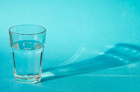 A glass with clean clear clear water stands on a blue background with green shadowsの写真素材