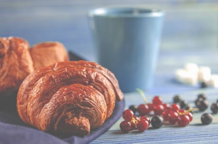Traditional French breakfast. Croissants with forest berries and a cup of coffee stands on a wooden...