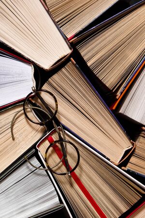 Many multicolored thick open books stand on a dark background. On the books are old round glasses. ready to readの写真素材